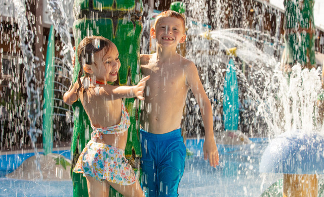 Kids under a water sprinkler - Stay & Splash 2022 - Waterpark Resorts