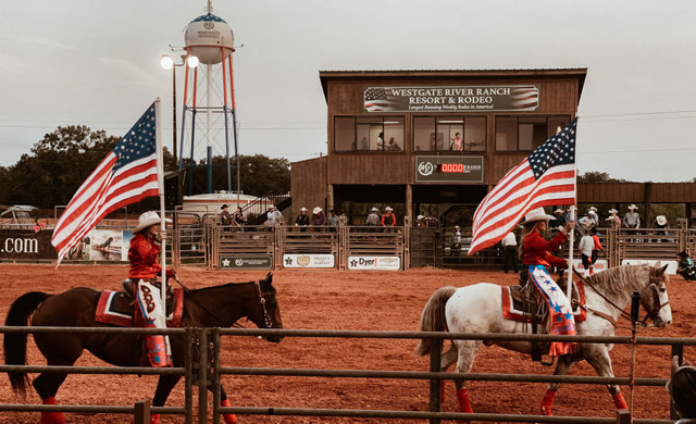 Two People Holding Flags In Rodeo Ring
